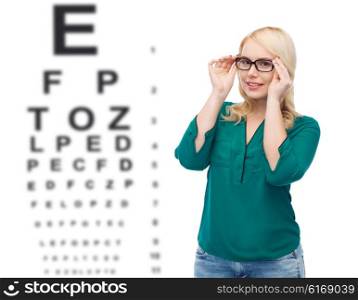 vision, ophthalmology, optics, health care and people concept - smiling young woman with eyeglasses over eye chart background