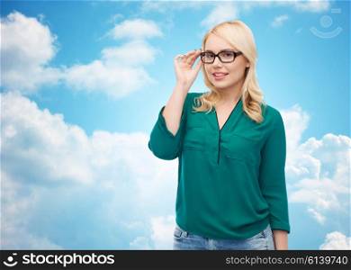 vision, optics, education and people concept - smiling young woman with eyeglasses over blue sky and clouds background