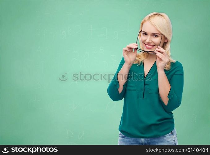 vision, optics, education and people concept - smiling young woman with eyeglasses over green school chalk board background