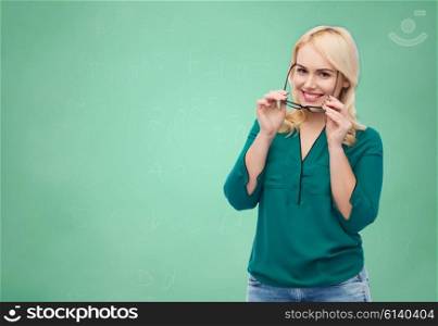 vision, optics, education and people concept - smiling young woman with eyeglasses over green school chalk board background