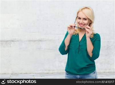 vision, optics, education and people concept - smiling young woman with eyeglasses over gray concrete wall background