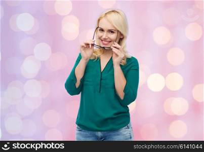 vision, optics, education and people concept - smiling young woman with eyeglasses over pink holidays lights background