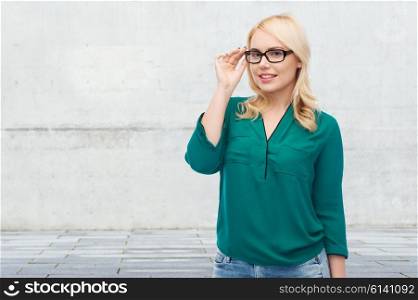 vision, optics, education and people concept - smiling young woman with eyeglasses over gray concrete wall background