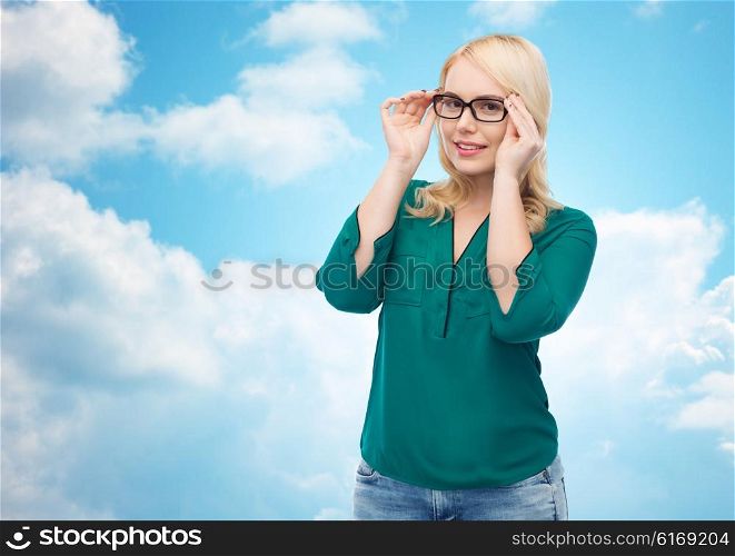 vision, optics, education and people concept - smiling young woman with eyeglasses over blue sky and clouds background