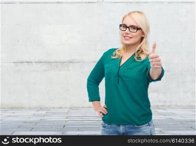 vision, optics, education, gesture and people concept - smiling young woman with eyeglasses showing thumbs up over gray concrete wall background