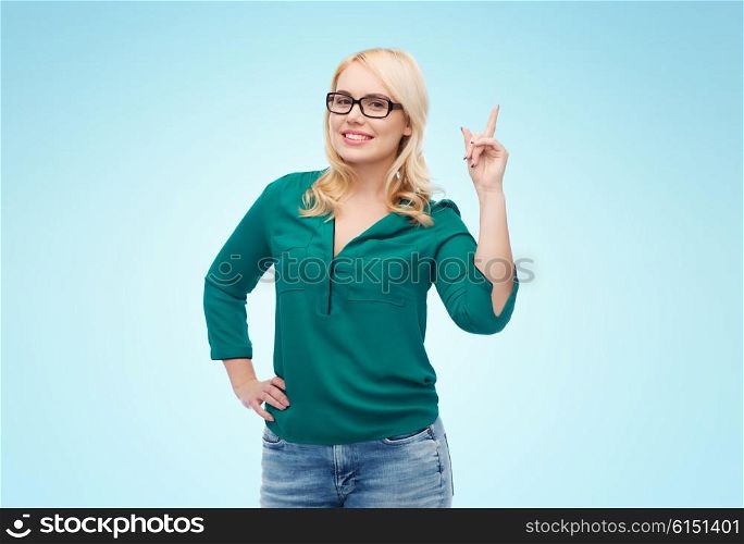vision, optics, education, gesture and people concept - smiling young woman with eyeglasses pointing finger up over blue background