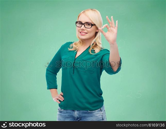 vision, optics, education, gesture and people concept - smiling young woman with eyeglasses showing ok over green school chalk board background