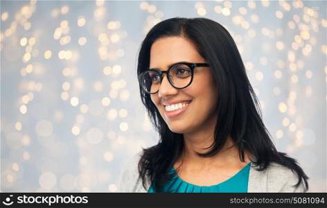 vision, portrait and people concept - happy smiling young indian woman in glasses over holidays lights background. happy smiling young indian woman in glasses