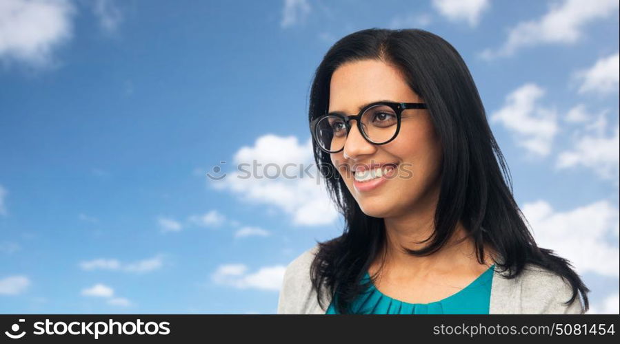 vision, portrait and people concept - happy smiling young indian woman in glasses over blue sky and clouds background. happy smiling young indian woman in glasses