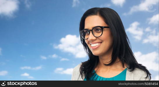 vision, portrait and people concept - happy smiling young indian woman in glasses over blue sky and clouds background. happy smiling young indian woman in glasses