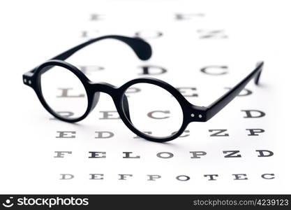 Vision screening. Old-fashioned round black eyeglasses, lying over the eye-checking chart