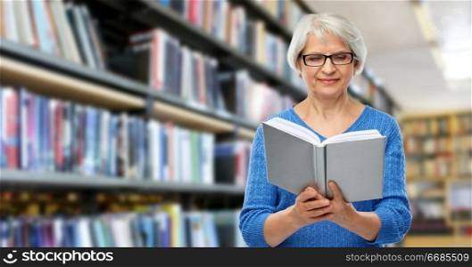 vision, wisdom and old people concept - smiling senior woman in glasses reading book over library background. senior woman in glasses reading book at library