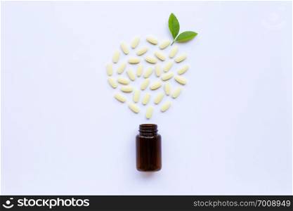 Vitamin C bottle and pills with green leavs on white background.