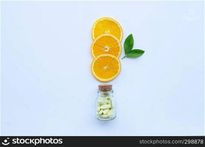 Vitamin C bottle and pills with orange fruit slices on white background.
