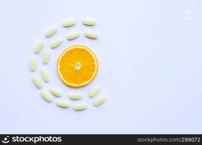 Vitamin C pills with orange fruit on white background.