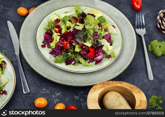 Vitamin salad with greens, pepper, red lettuce and cucumber, decorated with pomegranate.. Healthy salad of fresh vegetables and herbs.