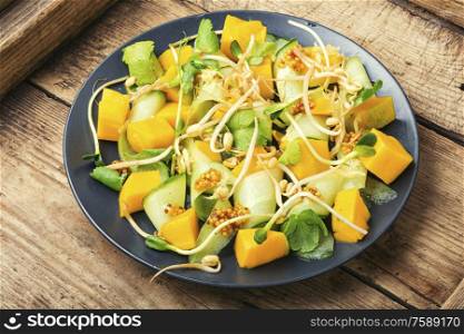 Vitamin spring salad with mango, cucumber and sprouts on old wooden table. Vegetable fruit salad with sprouts