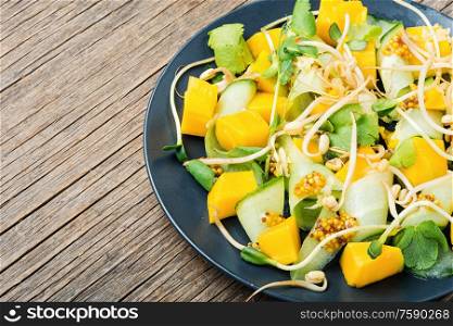 Vitamin spring salad with mango, cucumber and sprouts on old wooden table. Mix fruit and vegetable salad