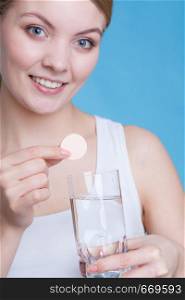 Vitamins, health, medicines. Woman holding glass with water and vitamin mineral supplement effervescent tablet. Studio shot on blue background. Woman holding glass with water and effervescent tablet