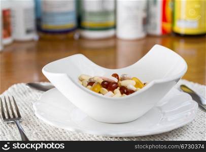 Vitamins in bowl of tablets for breakfast in kitchen with rows of bottles in background