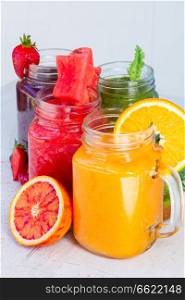 Vivid fresh smoothy drinks in glass jars with igredients on white table close up. Fresh smoothy drink with igredients