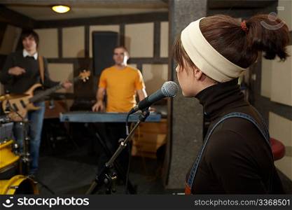 vocalist girl near microphone. focus on head of microphone. electro guitar player and keyboarder in out of focus