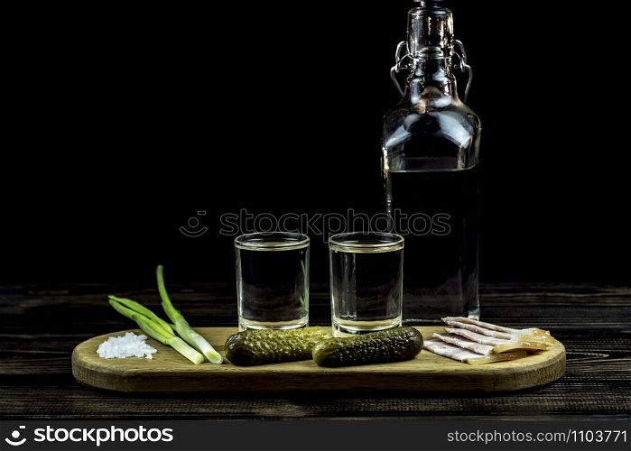 vodka and two glasses and cucumbers with bacon and onions