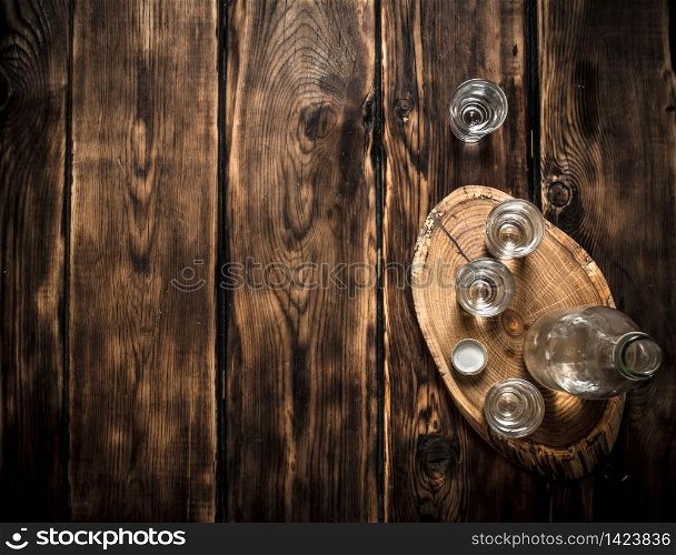Vodka bottle with shot glasses on the Board. On wooden background.. Vodka bottle with shot glasses on the Board.