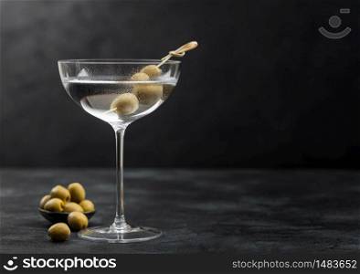 Vodka martini gin cocktail in modern glass with olives in metal bowl and bamboo sticks on black background.