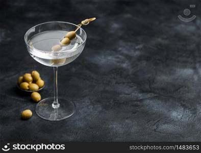 Vodka martini gin cocktail in modern glass with olives in metal bowl and bamboo sticks on black background.