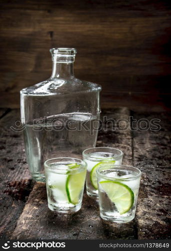 Vodka shots with ice and fresh lime. On a wooden background.. Vodka shots with ice and fresh lime.