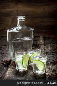 Vodka shots with ice and fresh lime. On a wooden background.. Vodka shots with ice and fresh lime.