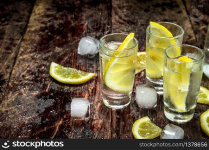 Vodka shots with ice and lemon. On a wooden background.. Vodka shots with ice and lemon.