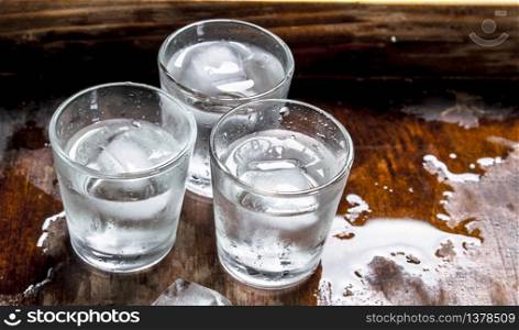 Vodka shots with ice on a wooden table.. Vodka shots with ice