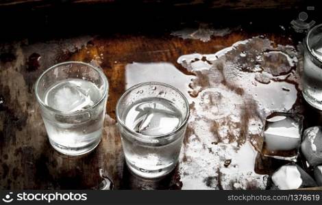 Vodka shots with ice on a wooden table.. Vodka shots with ice