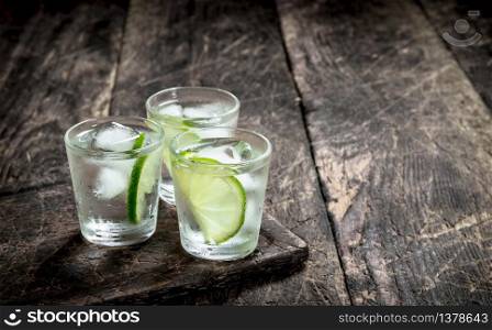 Vodka shots with lime and ice on the board. On a wooden background.. Vodka shots with lime and ice on the board.