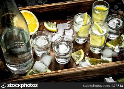 Vodka with lemon and ice on a wooden tray. Top view. Vodka with lemon and ice on a wooden tray.