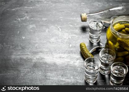 Vodka with pickled cucumbers. On a black wooden background.. Vodka with pickled cucumbers.