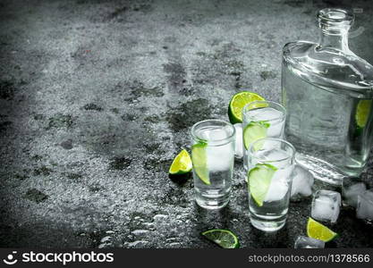 Vodka with pieces of lime and ice cubes. On a rustic background. Vodka with pieces of lime and ice cubes.