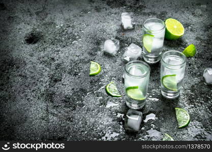 Vodka with pieces of lime and ice cubes. On a rustic background. Vodka with pieces of lime and ice cubes.