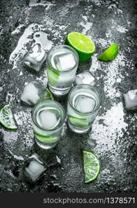 Vodka with pieces of lime and ice cubes. On a rustic background. Vodka with pieces of lime and ice cubes.