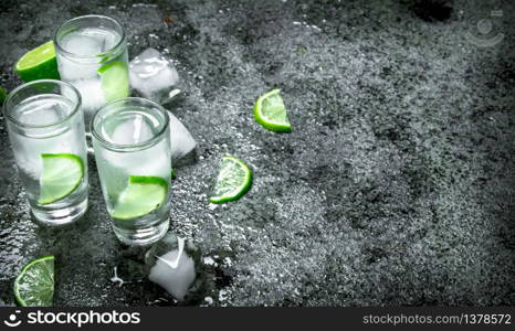 Vodka with pieces of lime and ice cubes. On a rustic background. Vodka with pieces of lime and ice cubes.