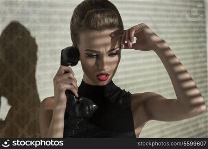 vogue creative portrait of sensual elegant woman talking with worried expression on phone in indoor half-light atmosphere