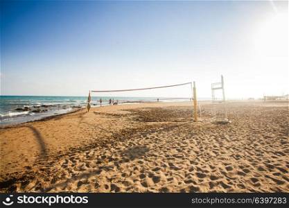 Volleyball net on sunny sandy beach with group of people in the background in summertime. Volleyball net. Activity recreation