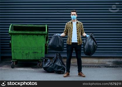 Volunteer in mask holds plastic trash bags outdoors, volunteering. People cleans city streets, ecological restoration, garbage collection and recycling, ecology care, environment cleaning. Volunteer in mask holds plastic trash bags