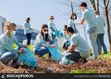 volunteering, charity and ecology concept - group of volunteers wearing face protective medical mask for protection from virus disease with garbage bags cleaning outdoor area. volunteers in masks with bags cleaning outdoors