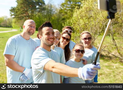 volunteering, charity and people concept - group of happy volunteers taking picture by smartphone and selfie stick in park. group of volunteers taking smartphone selfie