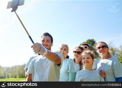volunteering, charity and people concept - group of happy volunteers taking picture by smartphone and selfie stick in park. group of volunteers taking smartphone selfie