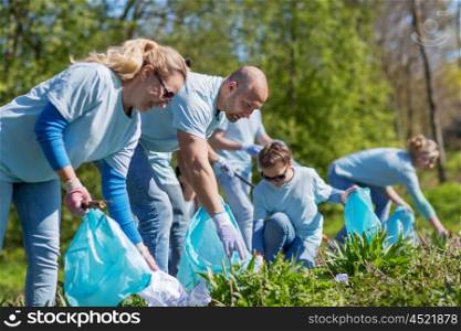 volunteering, charity, cleaning, people and ecology concept - group of happy volunteers with garbage bags cleaning area in park