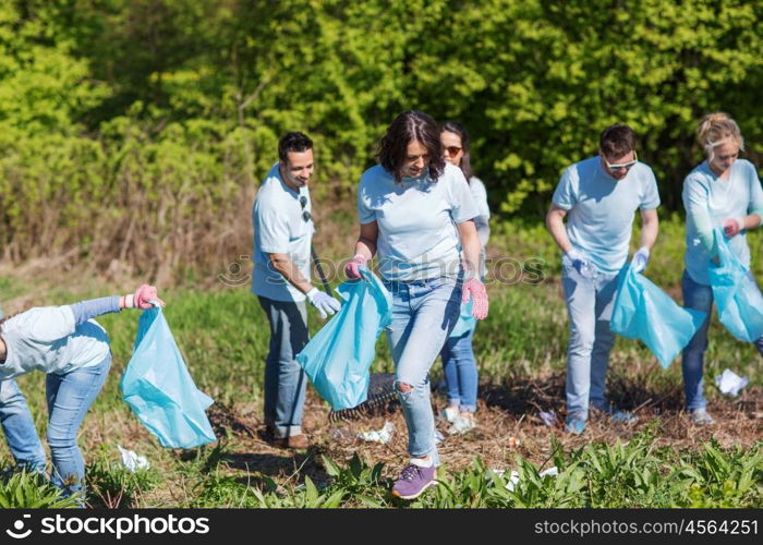 volunteering, charity, cleaning, people and ecology concept - group of happy volunteers with garbage bags cleaning area in park